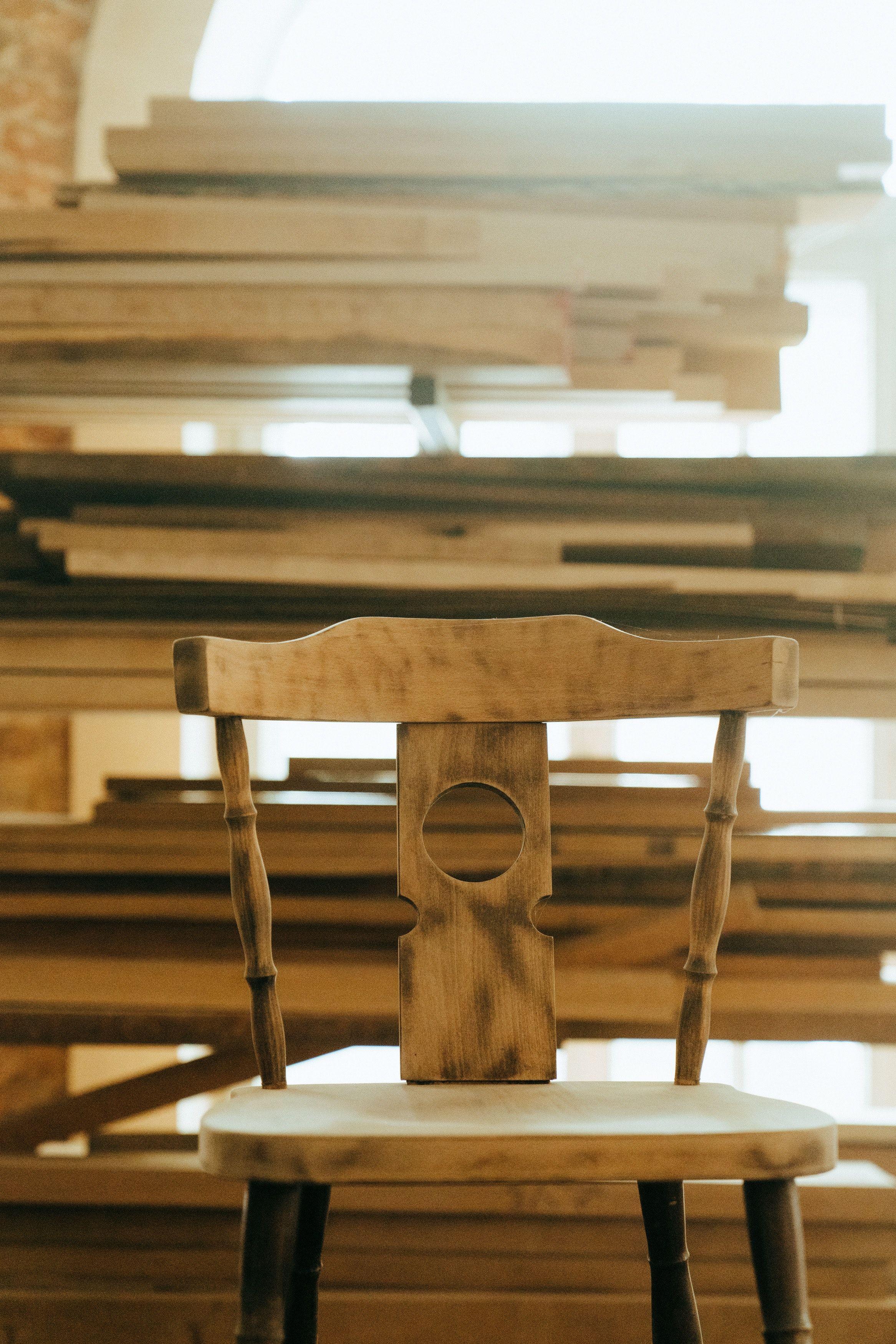 Handgefertigter Holzstuhl mit rundem Loch in der Rückenlehne steht in einer Schreinerwerkstatt vor gestapelten Holzbrettern.