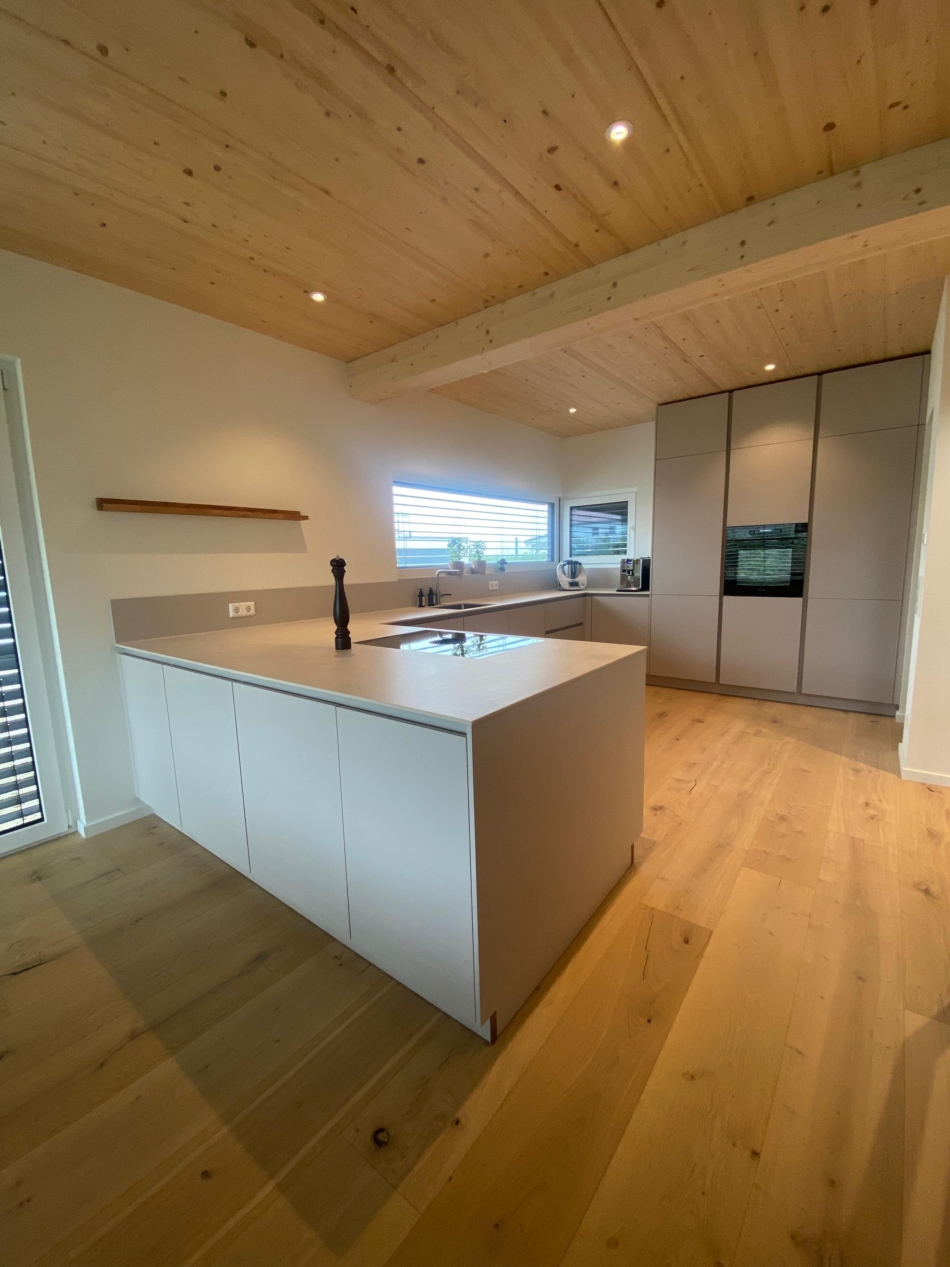 Moderne Kochinsel in sandfarbenen Tönen mit sichtbaren Holzbalken an der Decke und natürlichem Parkettboden
