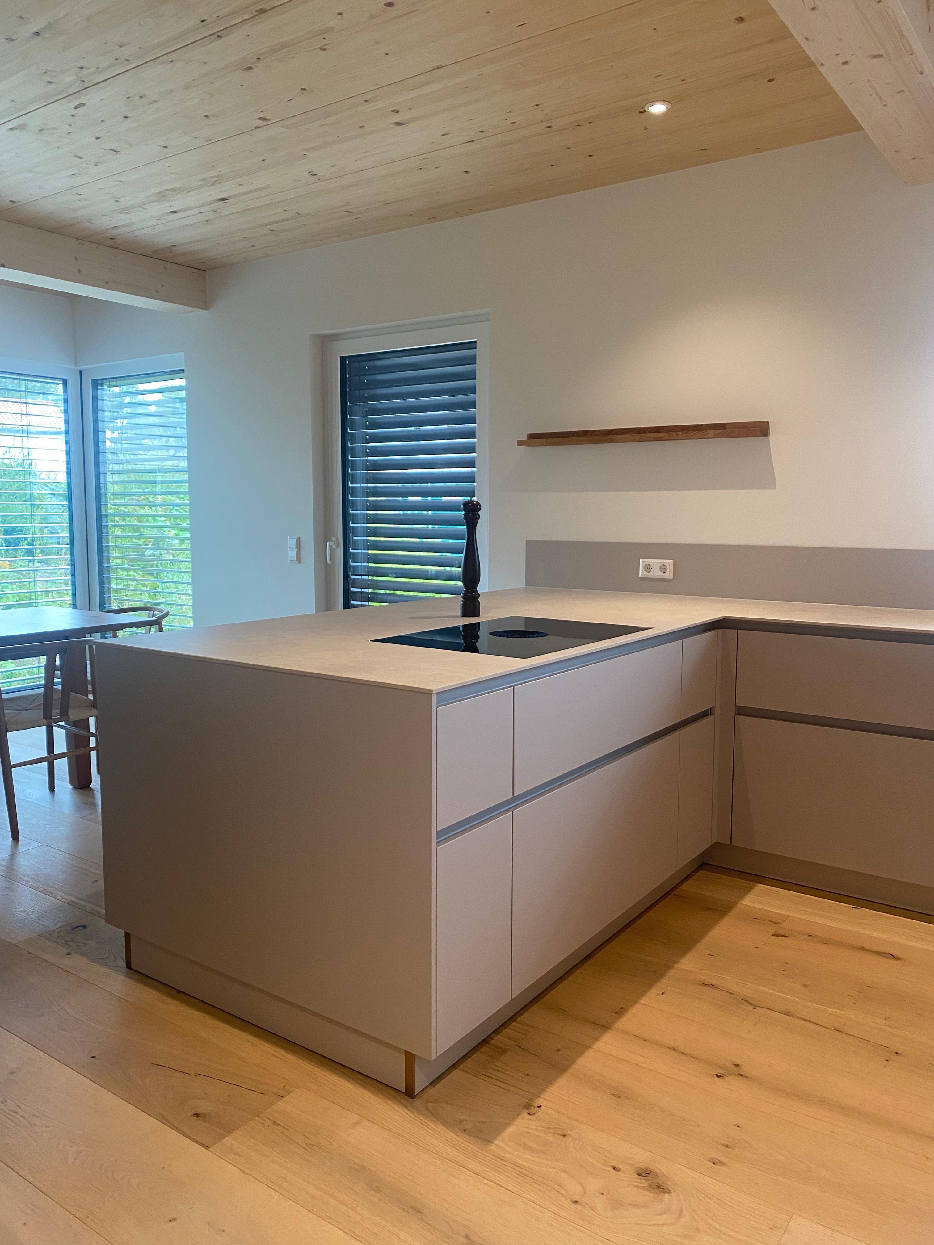 Sandfarbene Kücheninsel mit grifflosen Fronten, heller Arbeitsplatte und Induktionskochfeld in Landhaus-Ambiente