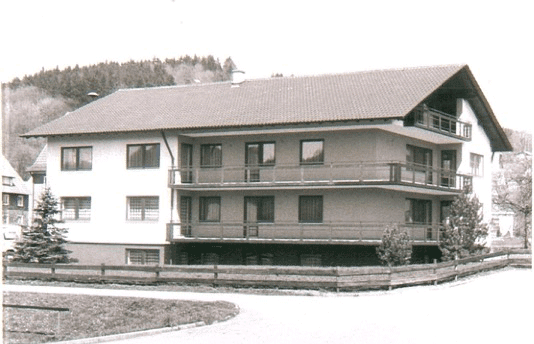 Historische Schwarz-Weiß-Fotografie eines modernen zweistöckigen Wohngebäudes mit Balkonen und Flachdach vor bewaldeter Hügellandschaft, vermutlich aus den 1970er Jahren.