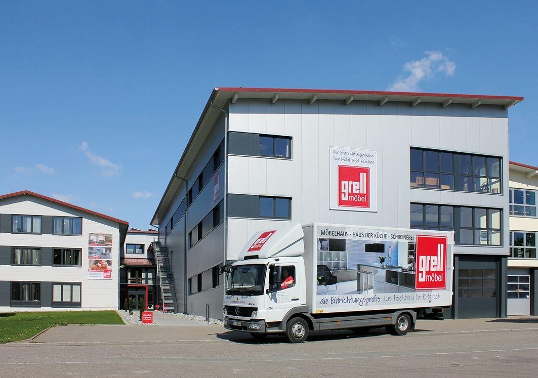 Modernes Möbelhaus "Grell Möbel" mit weißer Fassade und rotem Logo, vor dem ein Lieferwagen mit Firmenwerbung steht.