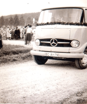 Historische Schwarz-Weiß-Fotografie eines Mercedes-Buses oder Transporters mit Menschengruppe im Hintergrund, vermutlich aus den 1960er Jahren.