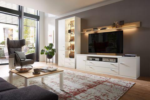 Moderne Wohnwand in Weiß mit Vitrine, TV-Element und Wandboard mit Beleuchtung – stilvoll eingerichtet in hellem Wohnzimmer mit Relaxsessel und Teppich.