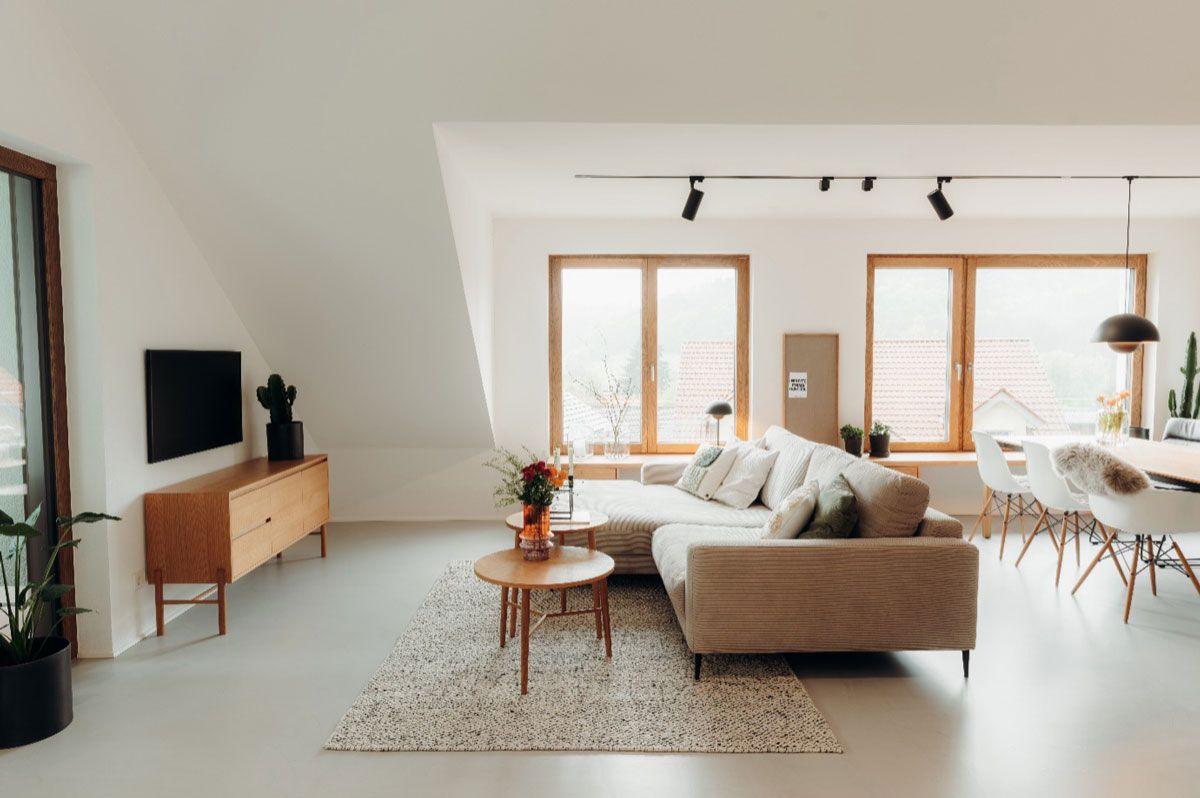 Modern, helles Wohnzimmer im skandinavischen Stil mit beiger Eckcouch, Holzmöbeln und großen Fenstern in offener Raumaufteilung.