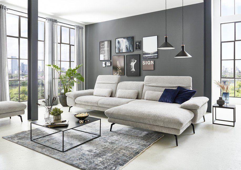 Graue Stoff-Eckgarnitur mit blauen Kissen vor grauer Galeriewand in Industrial-Loft-Ambiente.