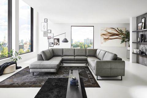 Große graue Leder-Wohnlandschaft in U-Form mit schwarzem Couchtisch vor Panoramafenstern in modernem Loft.