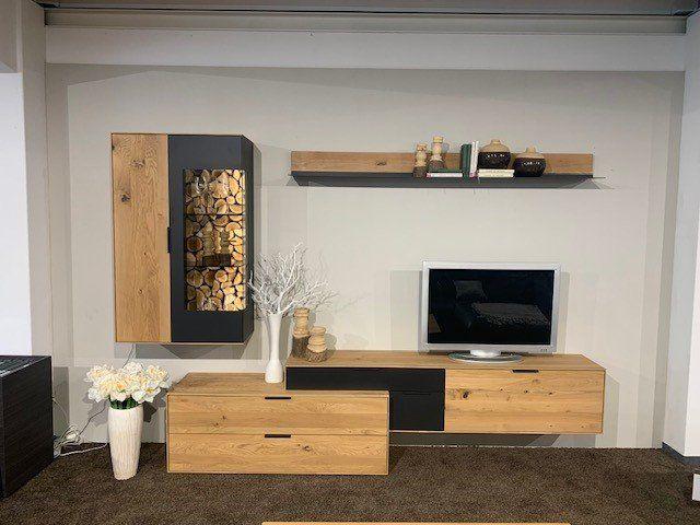 Moderne Wohnwand aus Holz und Anthrazit mit integriertem Brennholzfach und TV-Bereich.
