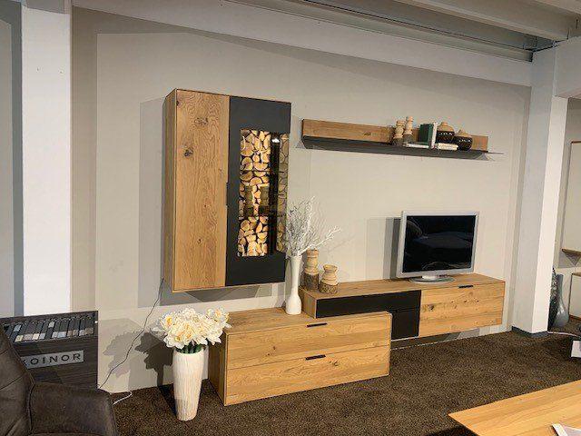 Holz-Wohnwand mit Brennholzlagerung, TV-Lowboard und dekorativen Elementen in Möbelhaus-Ausstellung.