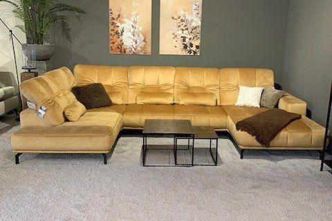 Große U-förmige Ledercouch in Senfgelb mit schwarzen Metallcouchtischen vor grauer Wand.