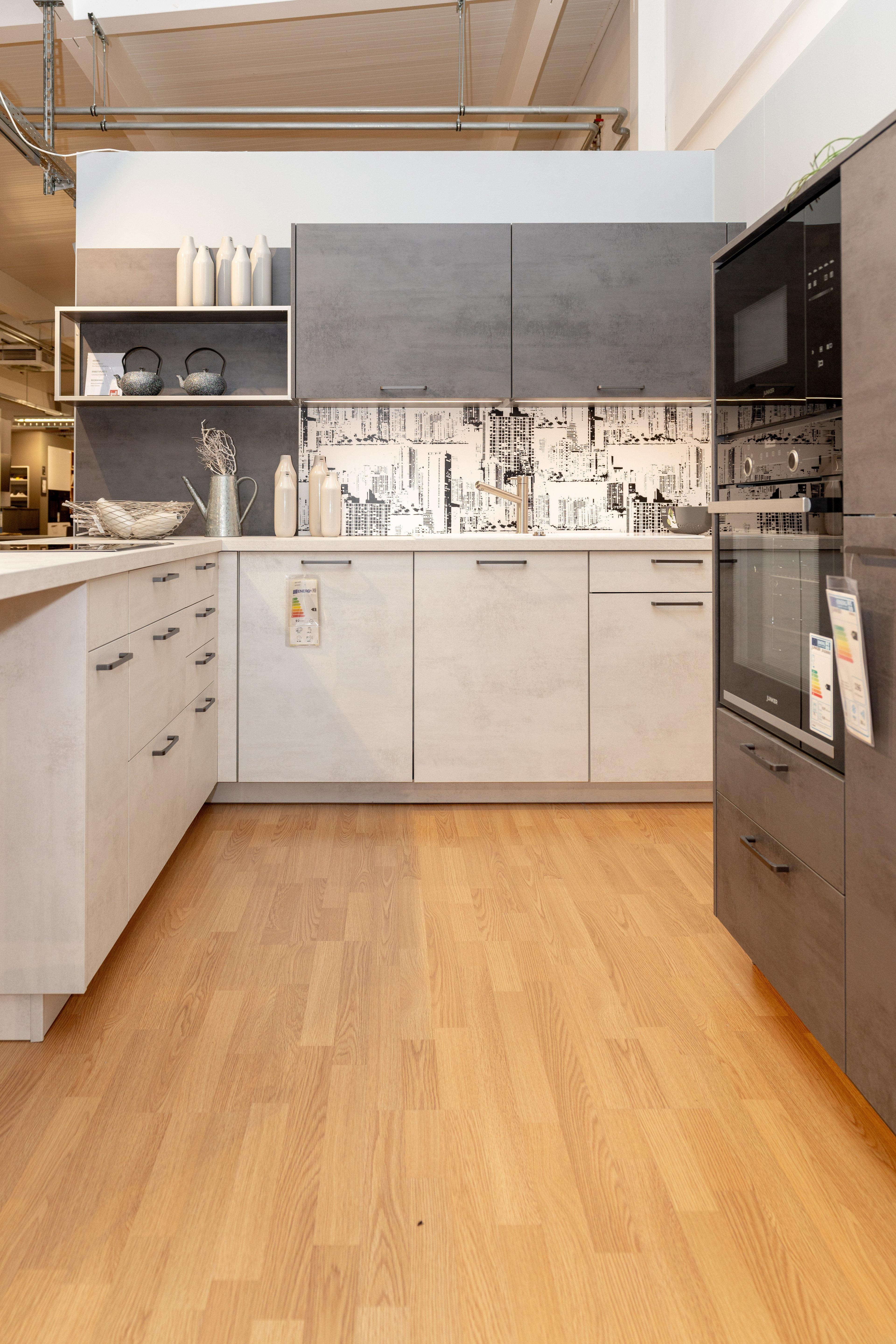 U-förmige Küche mit anthrazitfarbenen Oberschränken, hellen Unterschränken und Fliesenspiegel im Stadtdesign. Eingebaute Geräte und offene Regale mit weißen Flaschen und Geschirr, Parkett am Boden.
