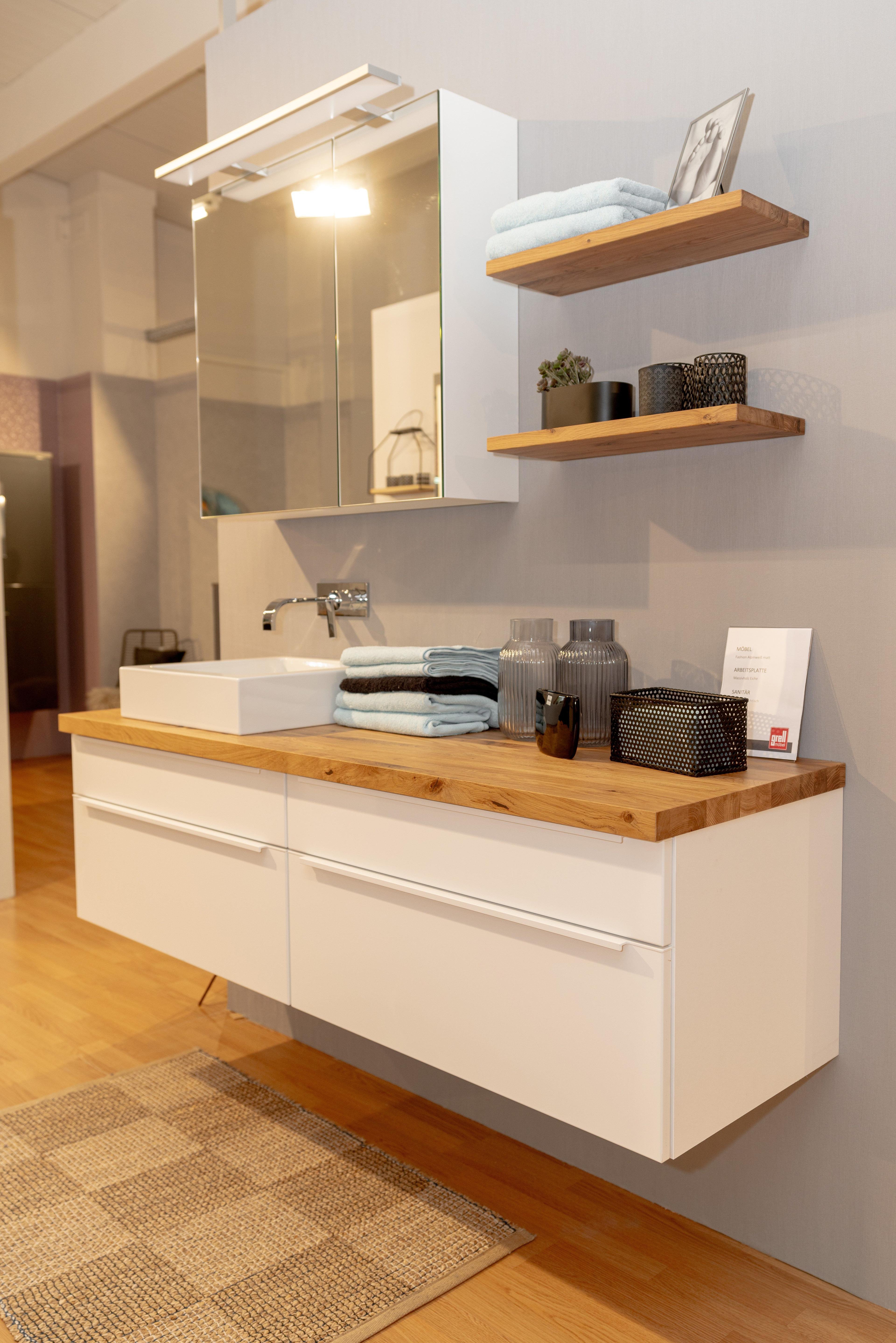 Nahaufnahme des Badmöbel-Sets mit weißem Aufsatzwaschbecken auf Eichenholzplatte, Wandarmatur und dekorativen Accessoires auf Holzregalen.