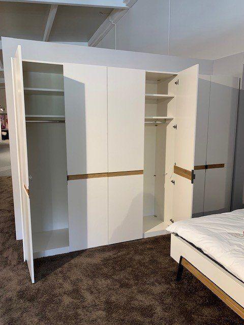 Geöffneter weißer Kleiderschrank zeigt Innenaufteilung mit Regalbrettern, Kleiderstangen und verschiedenen Fächern.
