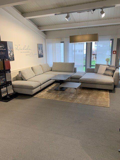 Große graue Stoff-Wohnlandschaft in U-Form mit schwarzem Couchtisch unter industrieller Holzbalkendecke.