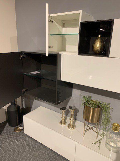 Wohnwand mit geöffneten Glasvitrinen und schwarzen Akzentfächern, dekoriert mit goldenen Accessoires.