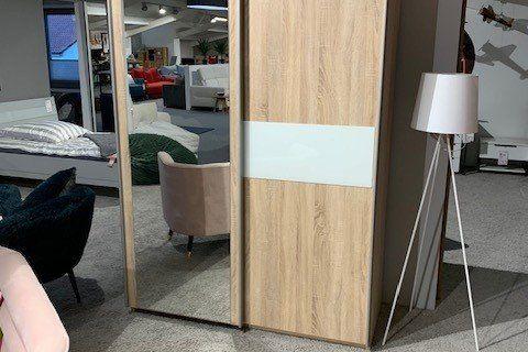Zweitüriger Kleiderschrank aus Eichenholz mit Spiegeltür und weißem Mittelstreifen in Möbelausstellung.
