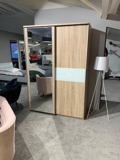 Zweitüriger Kleiderschrank aus Eichenholz mit Spiegeltür und weißem Mittelstreifen in Möbelausstellung.