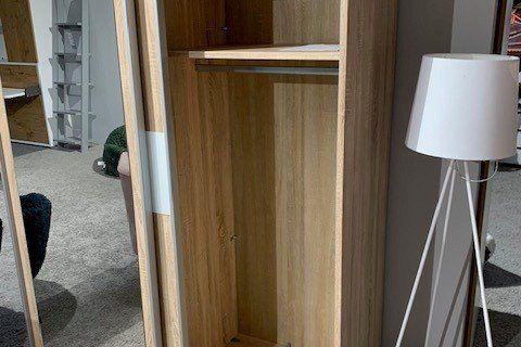 Zweitüriger Kleiderschrank aus Eichenholz mit Spiegeltür und weißem Mittelstreifen in Möbelausstellung.