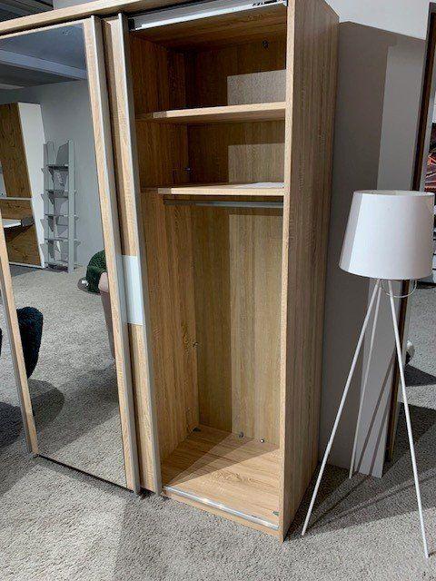 Geöffneter Kleiderschrank aus Eichenholz zeigt Innenaufteilung mit Regalboden und Kleiderstange.