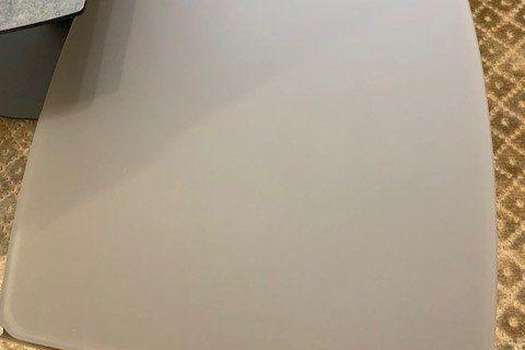 Weißer abgerunder Couchtisch mit matter Oberfläche auf goldfarbenem gemustertem Teppich, Detailaufnahme.
