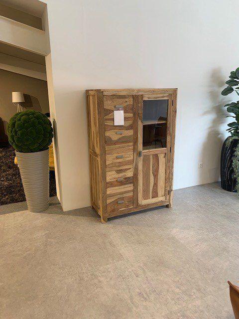 Rustikale Vitrine aus Massivholz mit Schubladen und Glastür in moderner Wohnzimmerausstellung mit Pflanzen.