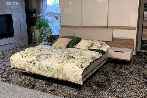 Modernes Schwebebett mit weißem Kopfteil und Überbau, Blumen-Bettwäsche und integrierten Nachttischen in Möbelausstellung.