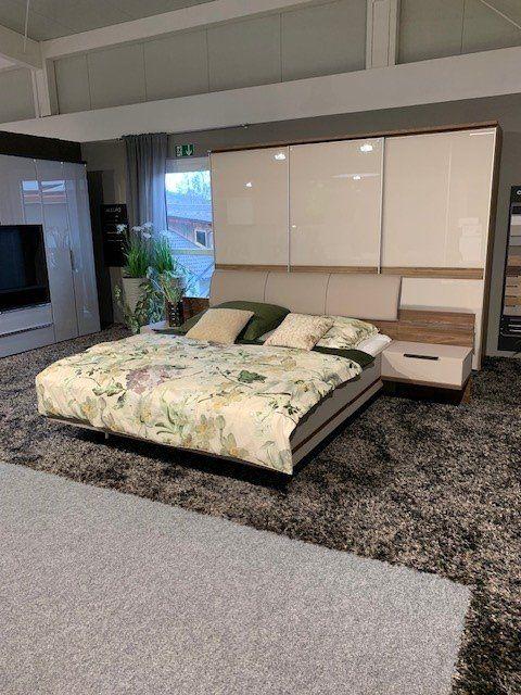 Modernes Schwebebett mit weißem Kopfteil und Überbau, Blumen-Bettwäsche und integrierten Nachttischen in Möbelausstellung.