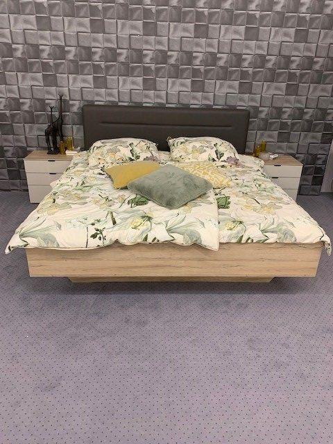 Doppelbett aus Eichenholz mit Blumen-Bettwäsche vor strukturierter grauer Wandverkleidung und weißen Nachttischen.
