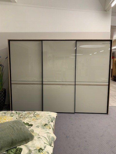 Dreitüriger Kleiderschrank mit grauen Glasfronten und Holzrahmen in moderner Möbelausstellung.
