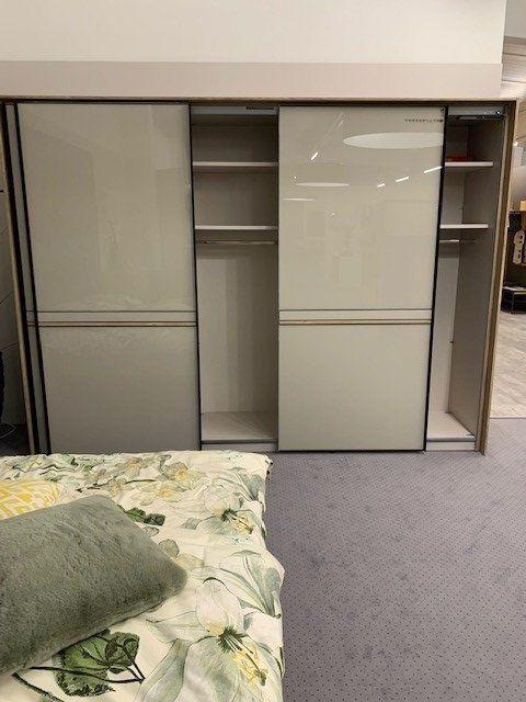 Geöffneter Kleiderschrank mit grauen Glasfronten zeigt Innenaufteilung mit Regalbrettern und Kleiderstangen.