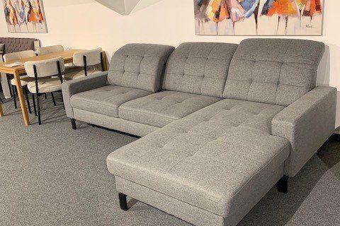Graue Stoff-Eckcouch mit Chaiselongue und dunklen Holzfüßen unter Dachschräge in Möbelhaus-Keller.