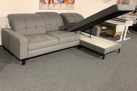 Graue Stoff-Eckcouch mit Chaiselongue und dunklen Holzfüßen unter Dachschräge in Möbelhaus-Keller.