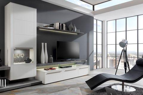 Moderne Wohnwand in Weiß und Grau mit TV, Regalen und schwarzem Relaxsessel vor großen Fenstern.