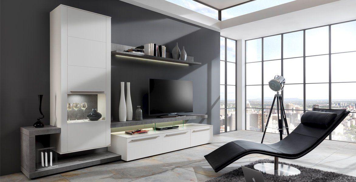 Moderne Wohnwand in Weiß und Grau mit TV, Regalen und schwarzem Relaxsessel vor großen Fenstern.