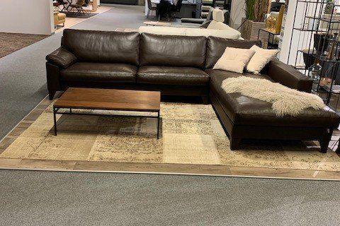 Schwarze Leder-Eckcouch mit Chaiselongue und Holz-Couchtisch in großem Möbelhaus-Showroom.