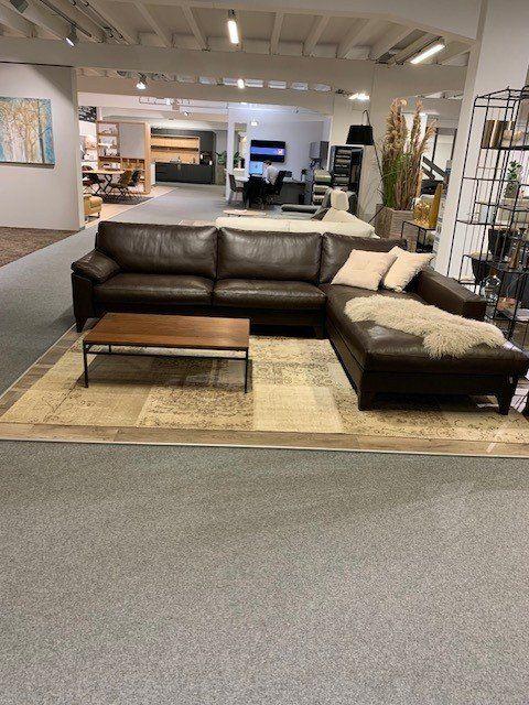 Schwarze Leder-Eckcouch mit Chaiselongue und Holz-Couchtisch in großem Möbelhaus-Showroom.