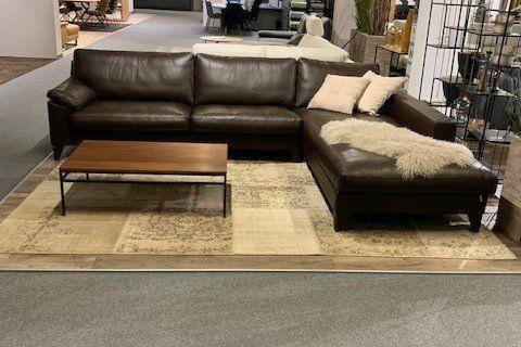 Schwarze Leder-Eckcouch mit Chaiselongue und Holz-Couchtisch in großem Möbelhaus-Showroom.