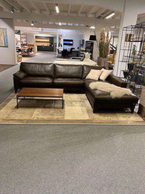Dunkelbraune Eckcouch aus Leder mit Fellkissen und Industrial-Couchtisch auf beigem Teppich.