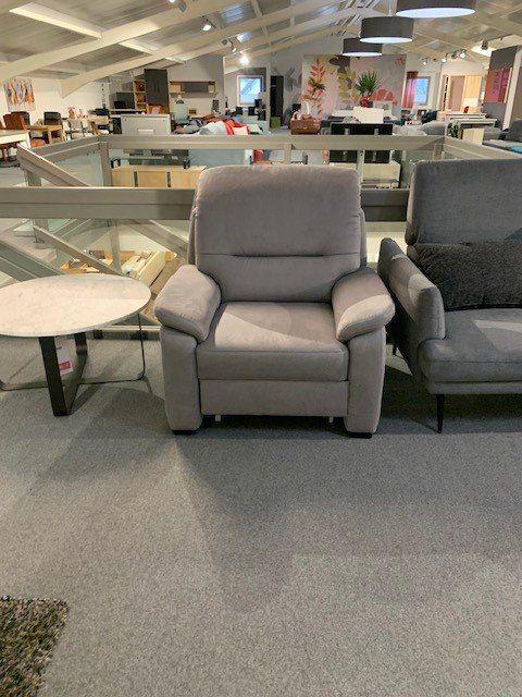 Klassischer grauer Sessel mit gepolsterten Armlehnen zwischen anderen Sitzmöbeln in Showroom.