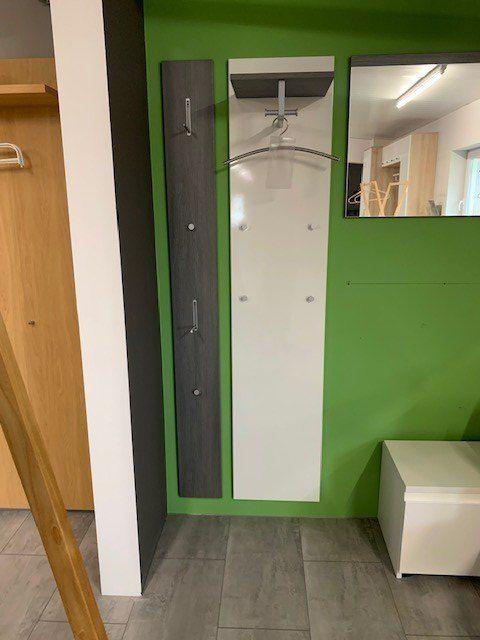 Detailansicht der Garderobe mit anthrazitfarbener Holzpanele, Kleiderhaken und weißer Spiegelfront.