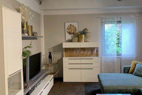Weiße Wohnwand mit TV-Bereich, Highboard und hellblauem Sofa unter sichtbarer Holzbalkendecke.