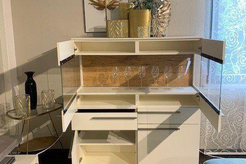Weiße Wohnwand mit TV-Bereich, Highboard und hellblauem Sofa unter sichtbarer Holzbalkendecke.
