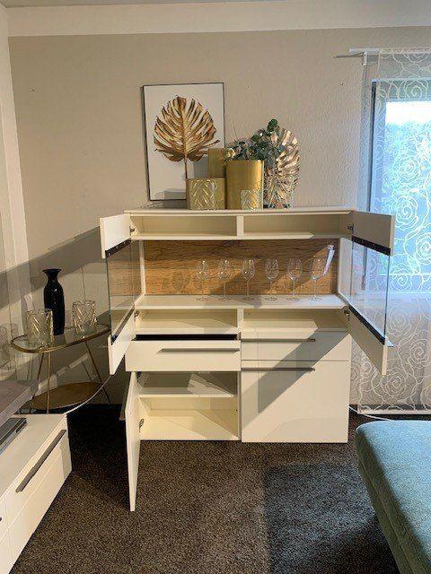 Weißes Highboard mit geöffneten Türen, Holzrückwand und goldenen Deko-Accessoires.