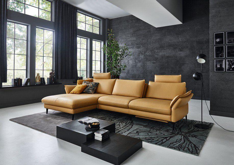 Luxuriöse Eckcouch in warmem Camel-Leder vor dramatischer Betonwand in modernem Loft-Ambiente.