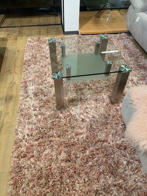 Glas-Couchtisch mit Metallgestell auf rosafarbenem Hochflor-Teppich in Möbelhaus-Ausstellung