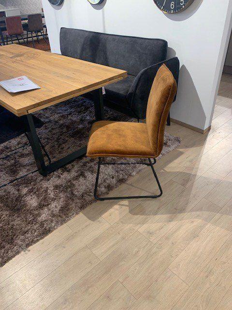 Cognacfarbener Lederstuhl auf schwarzem Kufengestell vor Holztisch mit dunkler Sitzbank in Möbelausstellung.