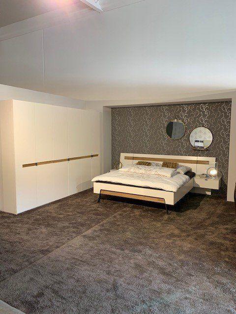 Elegantes Schlafzimmer unter Dachschräge mit weißem Bett, grauer Tapete mit Ornamentmuster und zwei runden Spiegeln.
