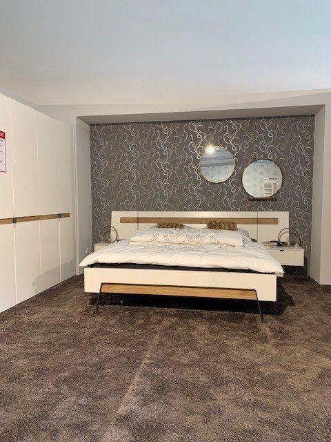Moderne Schlafzimmereinrichtung mit weißem Bett, dekorativen Rundspiegeln und ornamentaler Tapete in Grau.