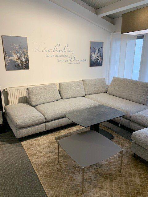 Moderne graue Eckcouch mit höhenverstellbarem Couchtisch vor weißer Wand mit Wandspruch.