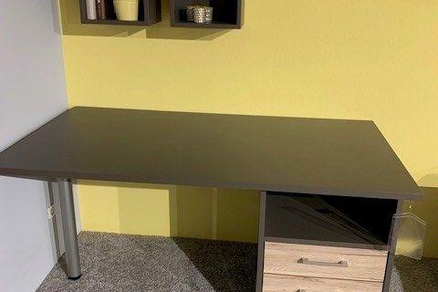 Eckschreibtisch in Anthrazit mit Holz-Schubladencontainer vor gelber Wand, darüber zwei schwarze Wandregale.