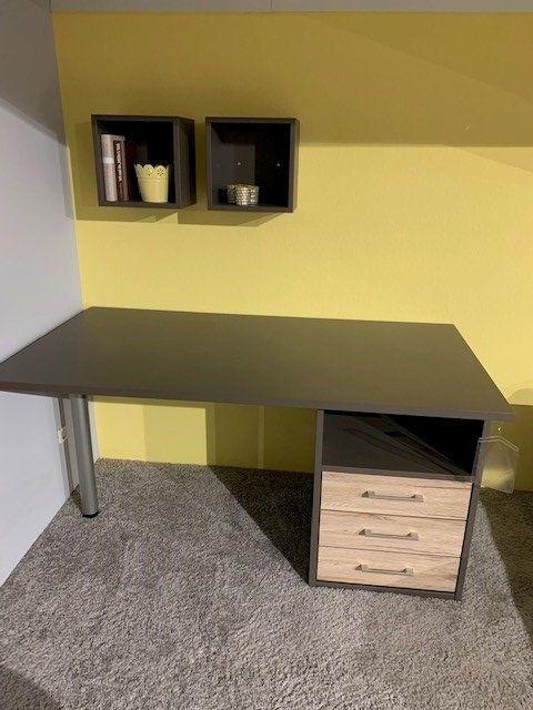 Eckschreibtisch in Anthrazit mit Holz-Schubladencontainer vor gelber Wand, darüber zwei schwarze Wandregale.